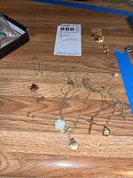 Photo of the lot on wooden surface showing multiple gold and gold filled necklaces with pendants, a pin, and loose small jewelry pieces.
