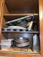 Wide shot showing all baking pans, kitchen tools and boxed Christmas cookie cutters stacked in a wooden shelf space.