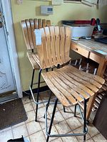 Two wooden slatted bar stools with black metal bases, showing wear and scratches on wood surfaces.