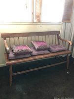 Wooden bench with three purple seat cushions and two decorative pillows in a well-lit room