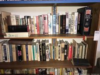 Books arranged on three wooden shelves, various titles shown including Holy Bible and multiple novels and nonfiction works