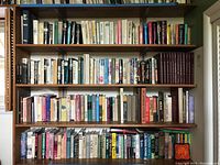 Bookshelf with a large assortment of hardcover and softcover books including visible titles in various genres.