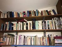 Three shelves filled with approximately 70 books of various genres including travel, fiction, nonfiction, novels, reference, parenting and religious books. Mixture of hardcover and softcover, mostly vintage to mid-sized books.