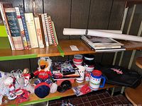 Shelved display showing an assortment of books, plush mascot, bobbleheads, mugs, a black Capitals bag, and small collectibles including pucks and pins