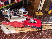 Photo showing four souvenir hockey sticks laid on floor with autographs and decals, several folded towels and rolled flags, Orioles tin can, and Redskins plastic helmet in the background.