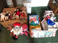 Wide view of lot showing boxes containing international dolls in traditional clothing, plush toys including Raggedy Ann and others, Care Bears carry case, assorted doll clothes, and other toys and items.