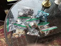 Multiple zip-top bags containing assorted jewelry pieces on glass table