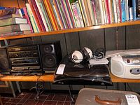 Shelf displaying black Sanyo stereo system with Bassound branded speakers, ION Profile LP USB turntable, white Aiwa boombox, and Lafayette headphones resting on turntable.