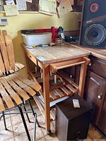 Side angle showing the wood kitchen cart with butcher block top, drawer, storage rack holding metal items underneath, and wheels