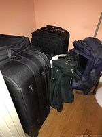 Photo showing several pieces of luggage grouped together, including two large black upright rolling suitcases, a small black carry bag, and two soft bags in navy and green/black colors