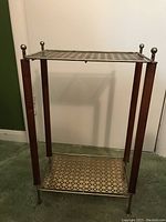 Vintage Mid Century Modern nightstand showing metal lattice top and bottom shelves supported by four wooden legs with metal finials and feet.