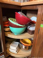Photo showing plastic mixing bowls in red, mint green, and beige stacked on a lazy Susan shelf with several plastic storage containers and lids.