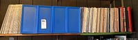 Photo of the front view showing a collection of vinyl records arranged vertically on a shelf along with three blue plastic storage boxes for vinyl albums.