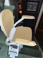 View of beige padded seat with armrests of Acorn Superglide 130 stair lift mounted on green-carpeted stairway.