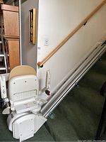 Side angle view showing beige seat, armrest, footrest, and straight metal rail installed on carpeted stairs.