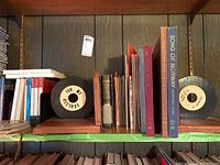 Shelf with various vinyl records held upright between wooden bookends, with children's story books including 'Song of Norway' visible on the right side.