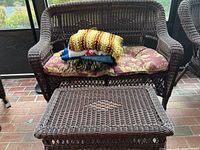 Wicker loveseat with seat cushion and folded afghans placed on top, wicker table in front.