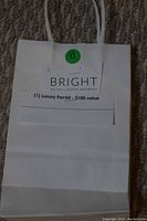 White paper bag with label showing $100 luxury facial from Bright Eye Spa Medical Aesthetics.