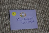 Photo shows a lavender envelope with handwritten text indicating the gift card from The Beach House Grill for $25, with a decorative cupcake sticker applied.