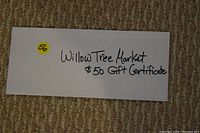 Photo of a white envelope labeled with 'Willow Tree Market $50 Gift Certificate' on a textured carpet.