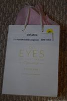 White gift bag with the text 'EYES Dr. Abby Jakob Optometrist' and contact info, including a note indicating donation of one pair of Guess sunglasses valued at $200.