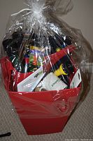 Overall view of the red planter filled with various gardening supplies wrapped in clear plastic.