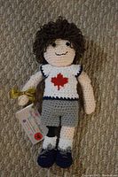 Photo of crochet Terry Fox doll showing front with maple leaf shirt, gray shorts, and curly hair