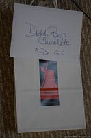 Photo shows a white envelope with handwriting indicating a $25 gift certificate from Dutch Boys Chocolate, placed over a Dutch Boys Chocolate paper bag.