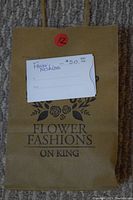 Photo shows a brown paper shopping bag with Flower Fashions on King logo and a $50 gift certificate placed on top of it.