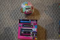 Photo shows a Mini LOL Surprise Family Ball and an unopened LOL Surprise Remix Pets Cube in original packaging on carpeted floor.