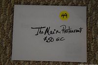 Photo of the front of a white envelope with handwritten text reading 'The Main Restaurant $50 G.C.' and a yellow sticker labeled '49'