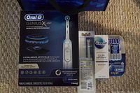 Boxed Oral-B Genius X electric toothbrush, travel case, brush heads, and Crest Gum Detoxify toothpaste arranged on carpet