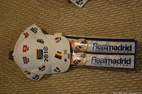 White Euro 2010 soccer cap printed with country flags and two pairs of Real Madrid club de futbol clapper sticks lying on carpeted floor.
