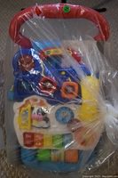 VTech Sit-to-Stand Learning Walker wrapped in plastic, showing interactive colorful features including a piano keyboard and animal figures.