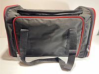 Closed view of a black fabric pet carrier with red trim and carrying handles
