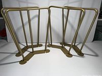 Four gold-tone metal hairpin legs standing on a white surface, showing the shape and structure clearly.
