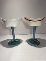 Two vintage nurse caps displayed on separate stands, one plain white and one with red trim.