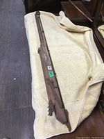 Full view of long wooden and metal antique carpet stretcher tool resting on beige cloth, showing length and overall shape.