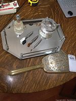 Full view of dresser set on wooden table showing mirrored holder with perfume bottle, canister, brushes, and large ornate hand mirror.