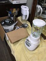 Wide shot showing all items including blender, rice cooker, Brita pitcher, utensils in canister, and measuring cups in cardboard box