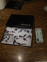Original Shepherds box containing purple beaded necklace and matching earrings with additional earrings displayed on a block next to the box