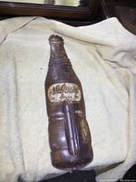 Front and side views of the vintage NuGrape metal thermometer shaped like a soda bottle. Shows embossed logo, thermometer and surface rust.