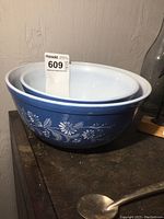Pair of two mixing bowls stacked, one larger medium blue with white floral design, smaller plain white bowl inside.
