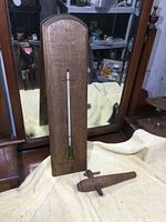 Wooden vintage thermometer standing vertically with round top and visible glass tube. Wooden spigot laying beside it on a yellow cloth.