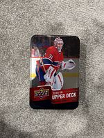 Metal tin container showing the cover of the 2015-16 Series 1 Upper Deck hockey card set, with image of a goalie in red and white uniform.