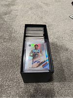 Top-down image of a black ETB box filled with NBA basketball cards, focusing on one card with a player in a Sacramento Kings jersey, holographic and autograph features visible.