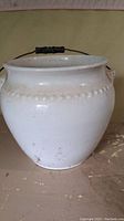 Side view of white ceramic chamber pot showing bead pattern and metal wire handle with black grip.