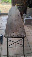 Long wooden plank ironing board top with visible cracks and holes, supported by metal legs.