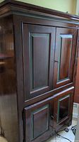 Full view of the brown wooden cabinet/armoire with green trim, showing doors and molding