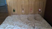 Four clear glass tumblers each with a different 3D holiday character: Christmas tree, snowman, candy cane, and Santa Claus.
